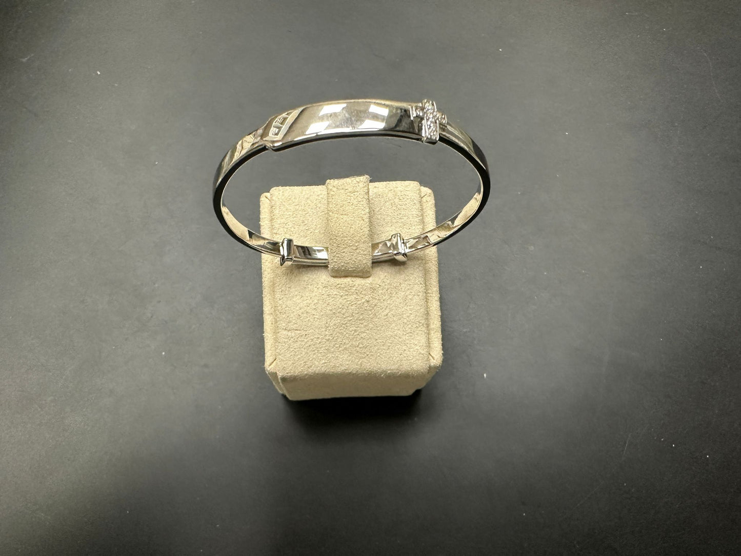 Sterling silver children's cross bangle displayed on a soft beige jewelry holder.