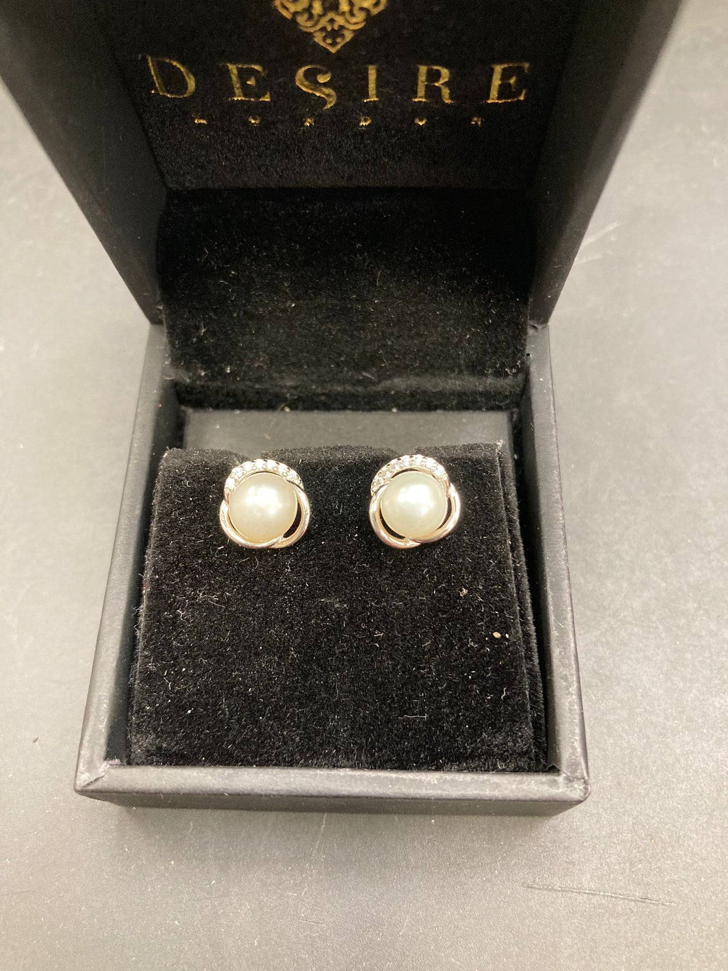 Sterling silver pearl stud earrings displayed in a black jewelry box with velvet lining.