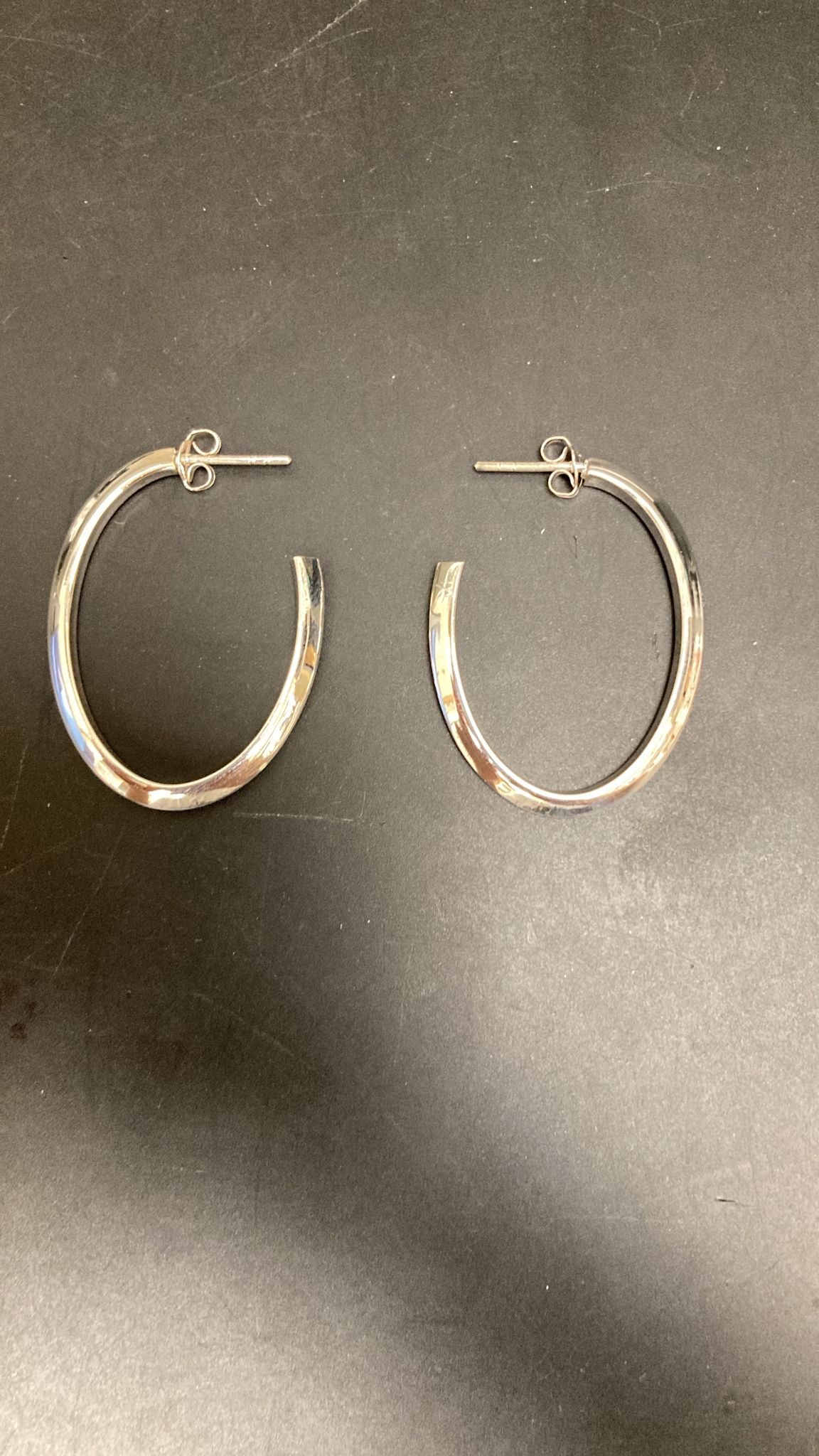 Sterling Silver Open Hoop Earrings EP019250485 lying on a dark surface, showcasing their elegant design.