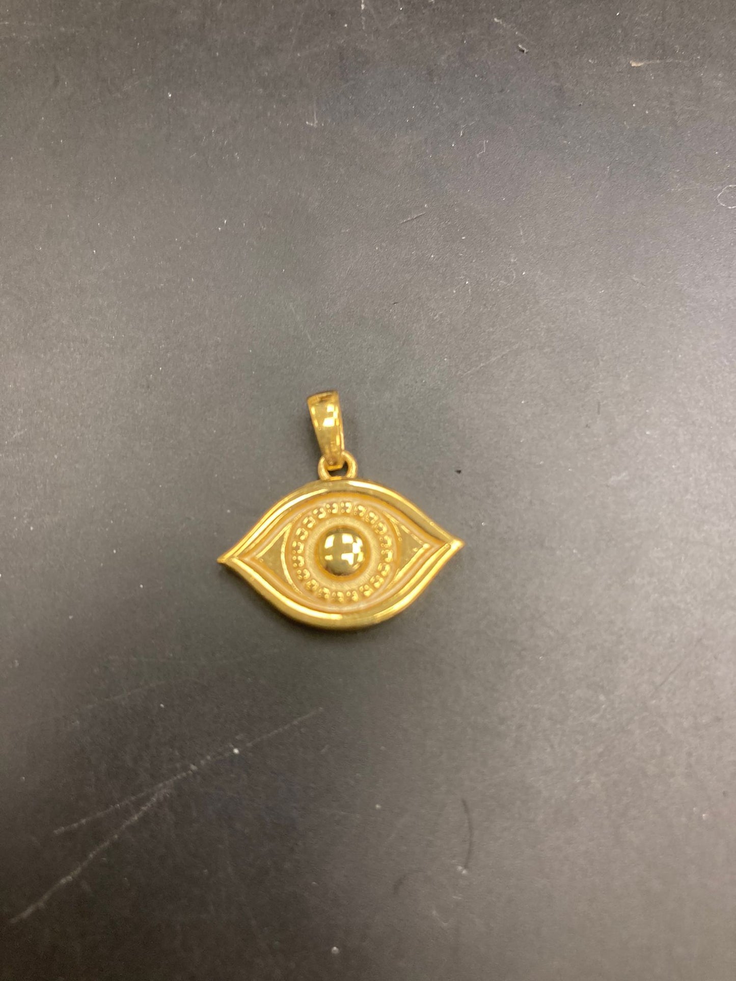 Gold eye pendant with intricate detailing on a dark background