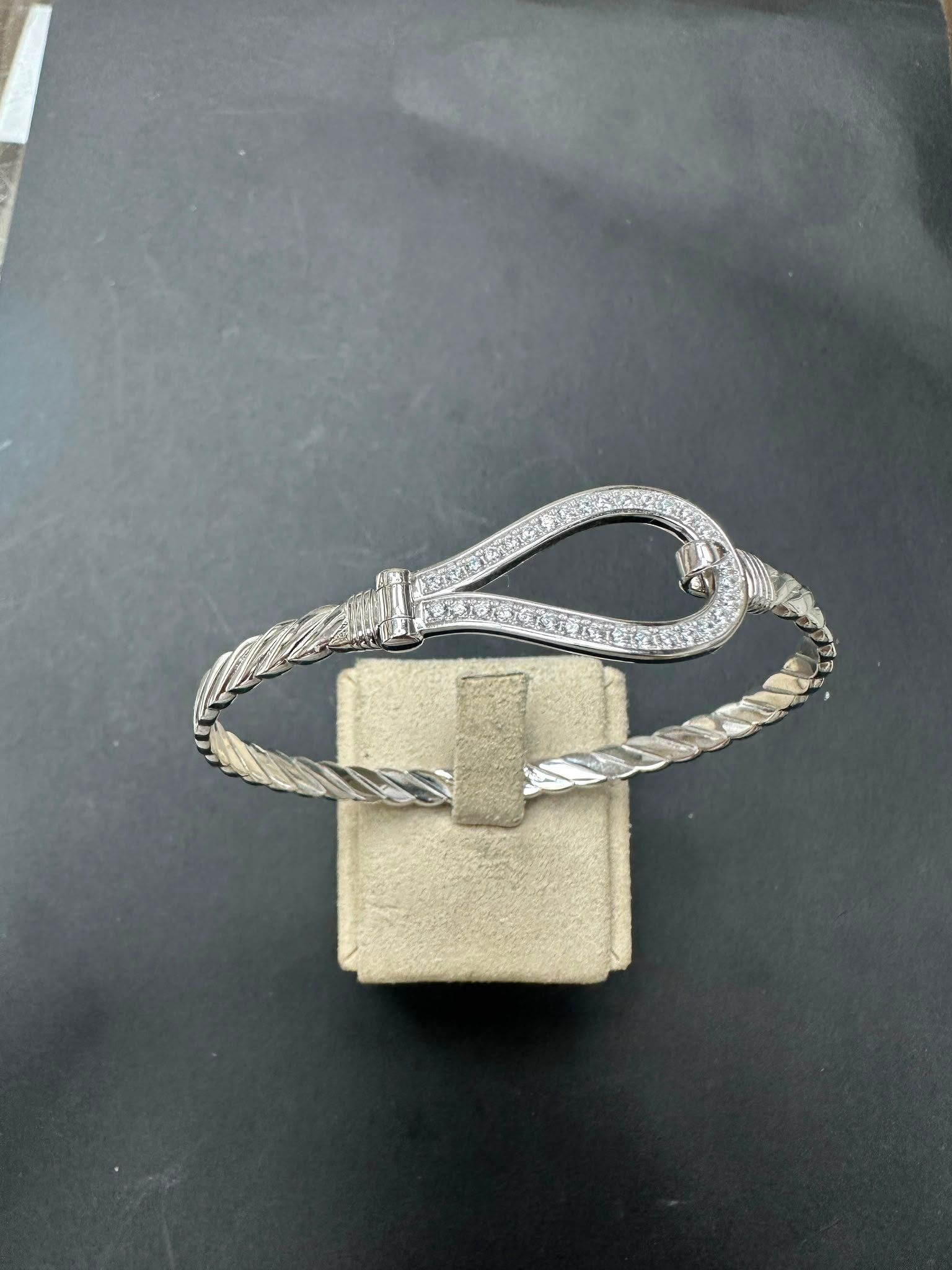 Sterling silver horseshoe bangle with CZ stone, designed with braided details, displayed on velvet stand.