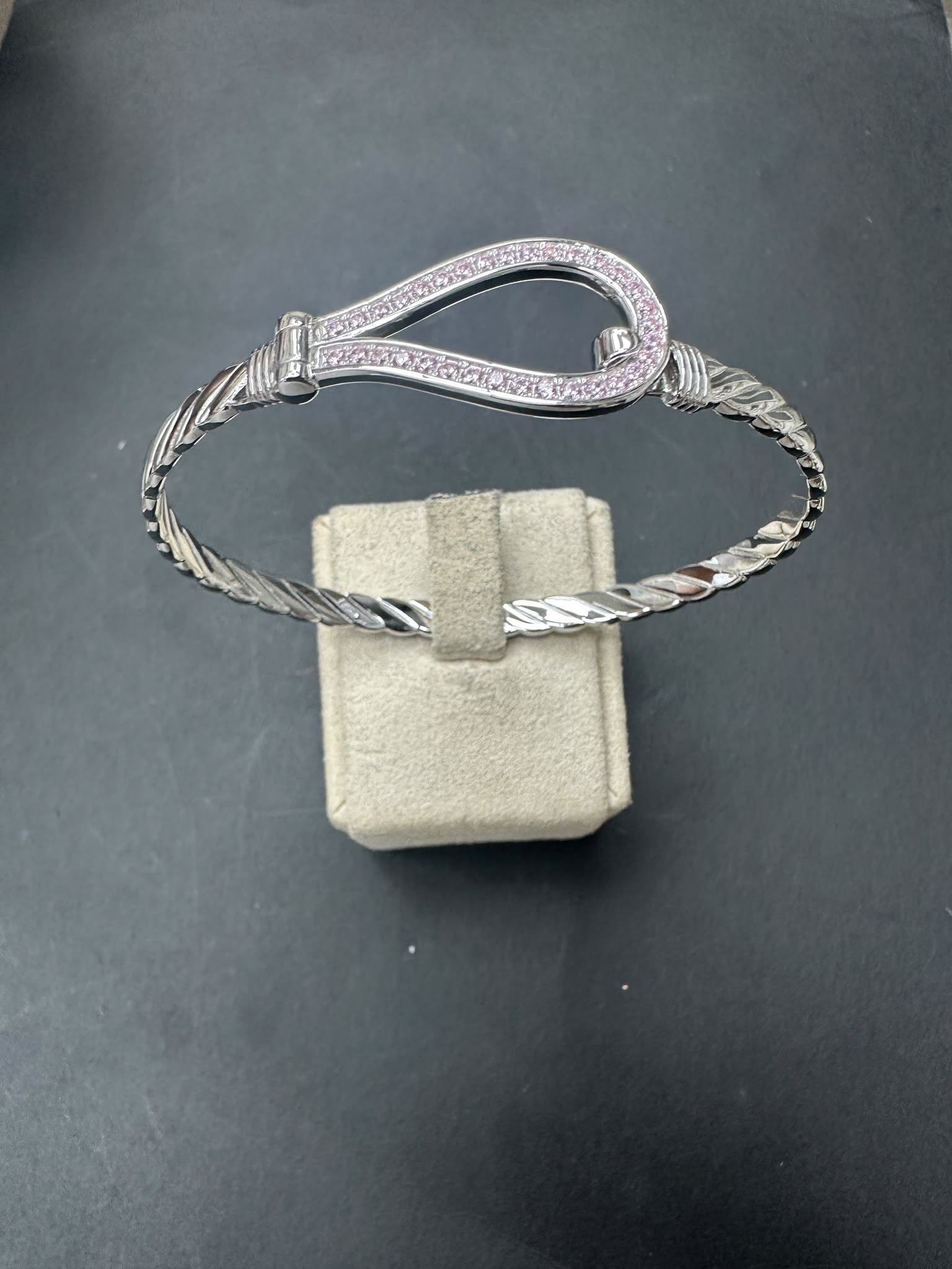 Sterling silver horseshoe bangle with pink cz stone, elegantly displayed on a gray velvet box.