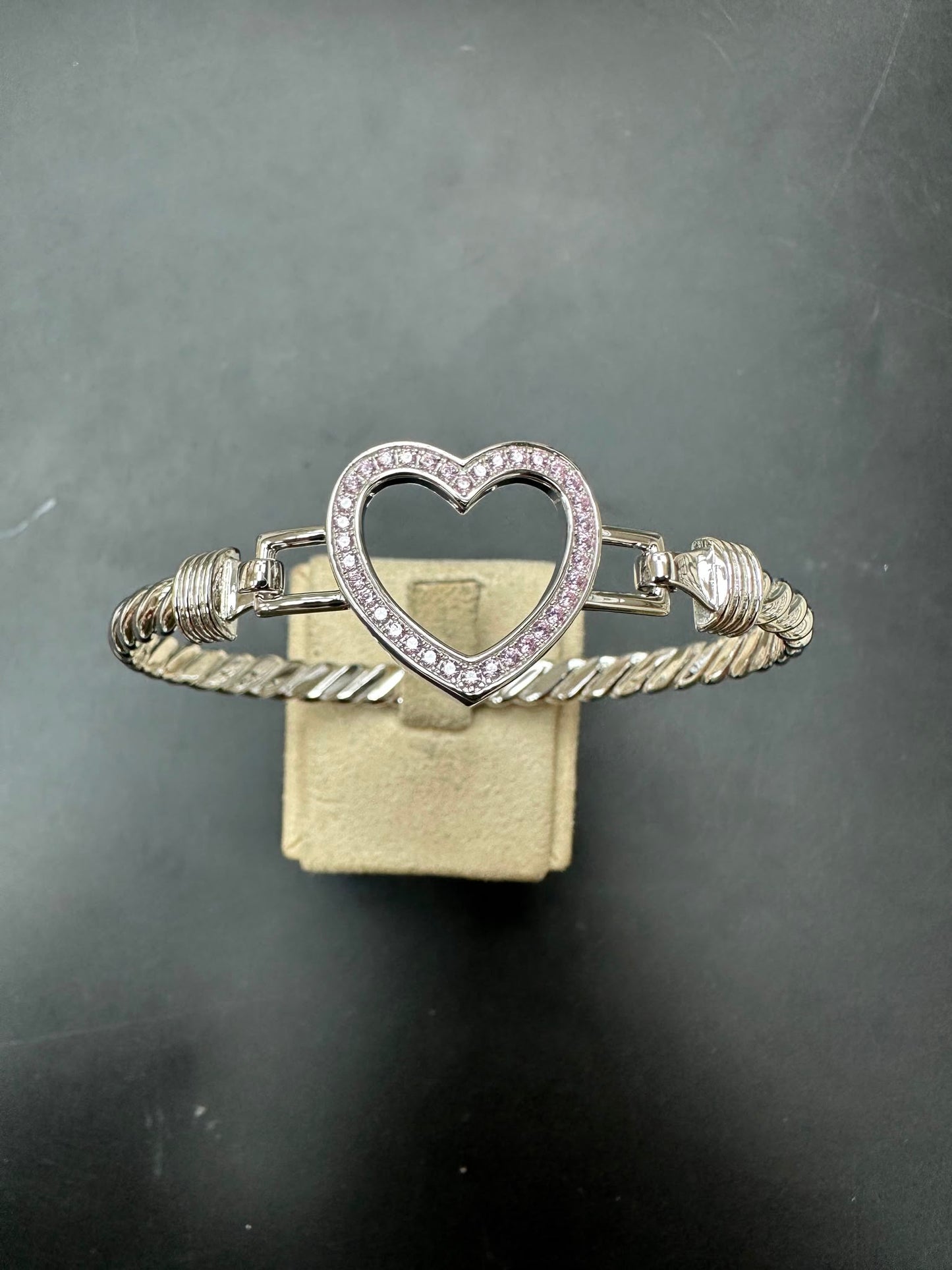 Sterling silver open heart bangle with pink CZ stones displayed on a stand.