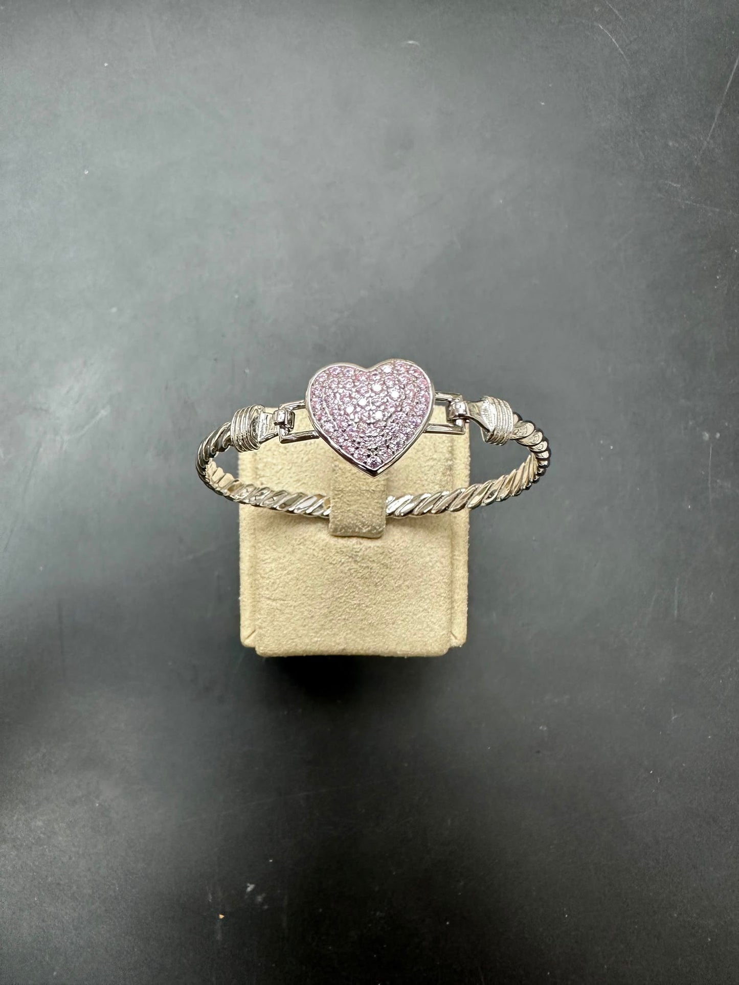 Sterling silver heart bangle with pink cz stone, size 4mm, displayed on a beige box against a dark background.