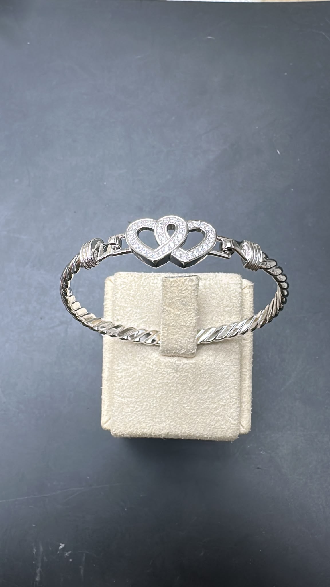 Sterling silver double heart bangle with sparkling hearts on a display stand, elegantly designed in white.