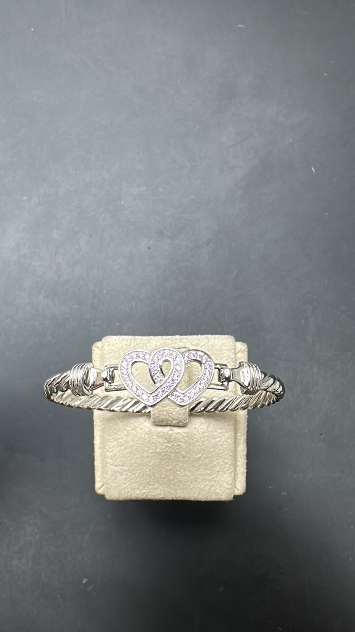 Sterling silver double heart bangle with pink accents on a display stand.