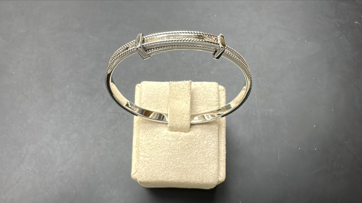 Sterling silver children's bangle resting on a display, 4.30mm thick and 50mm wide, featuring a milgrain design.