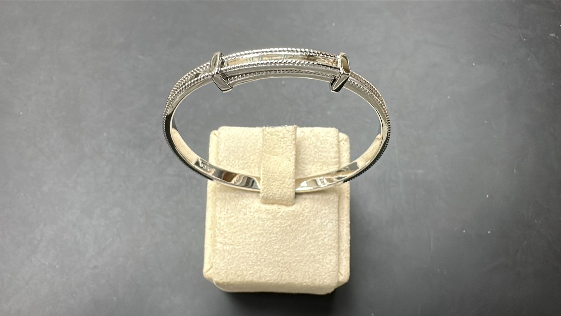 Sterling silver children's bangle resting on a display, 4.30mm thick and 50mm wide, featuring a milgrain design.