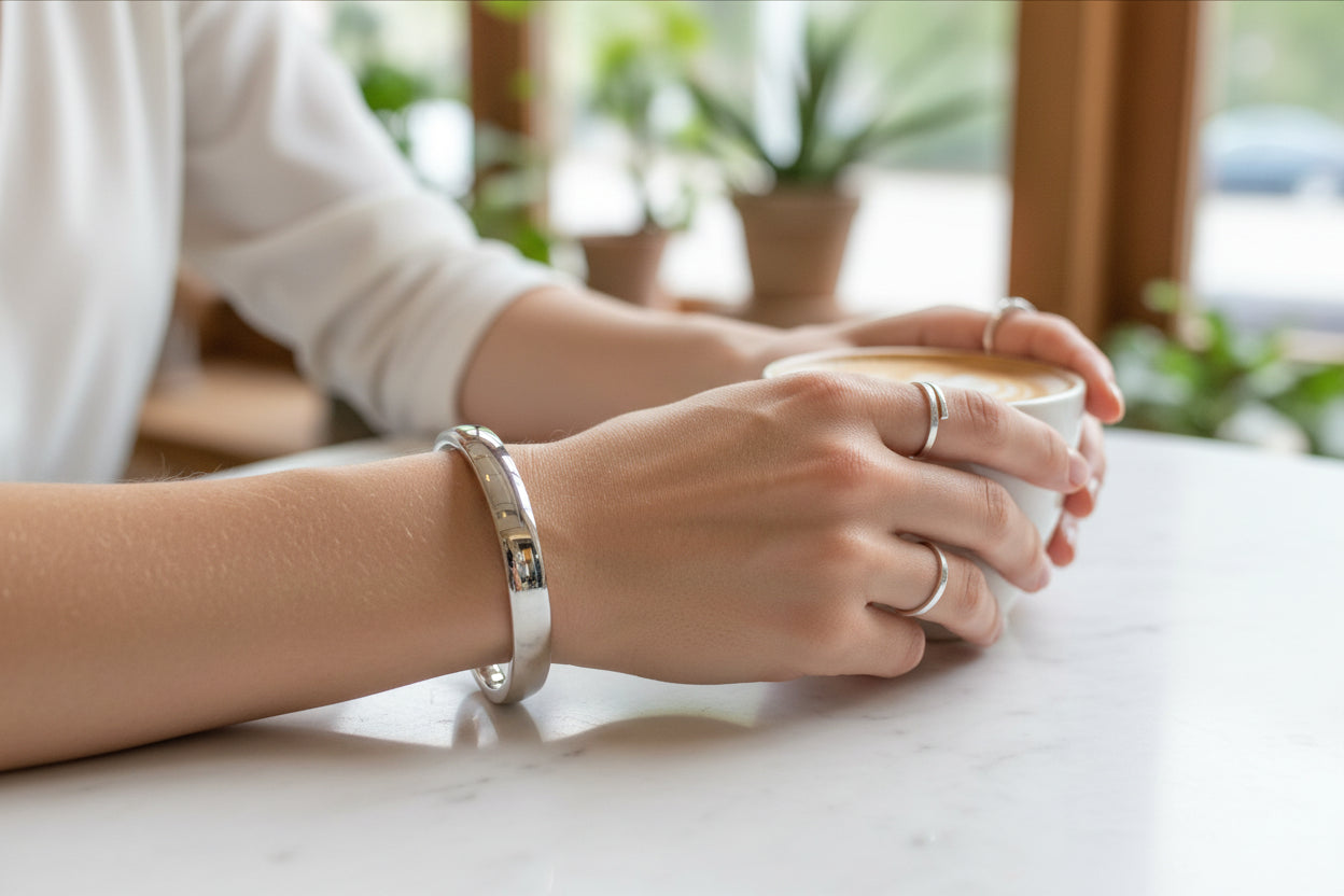 Model wearing a sterling silver hinged bangle while holding a cup of coffee on a marble table.