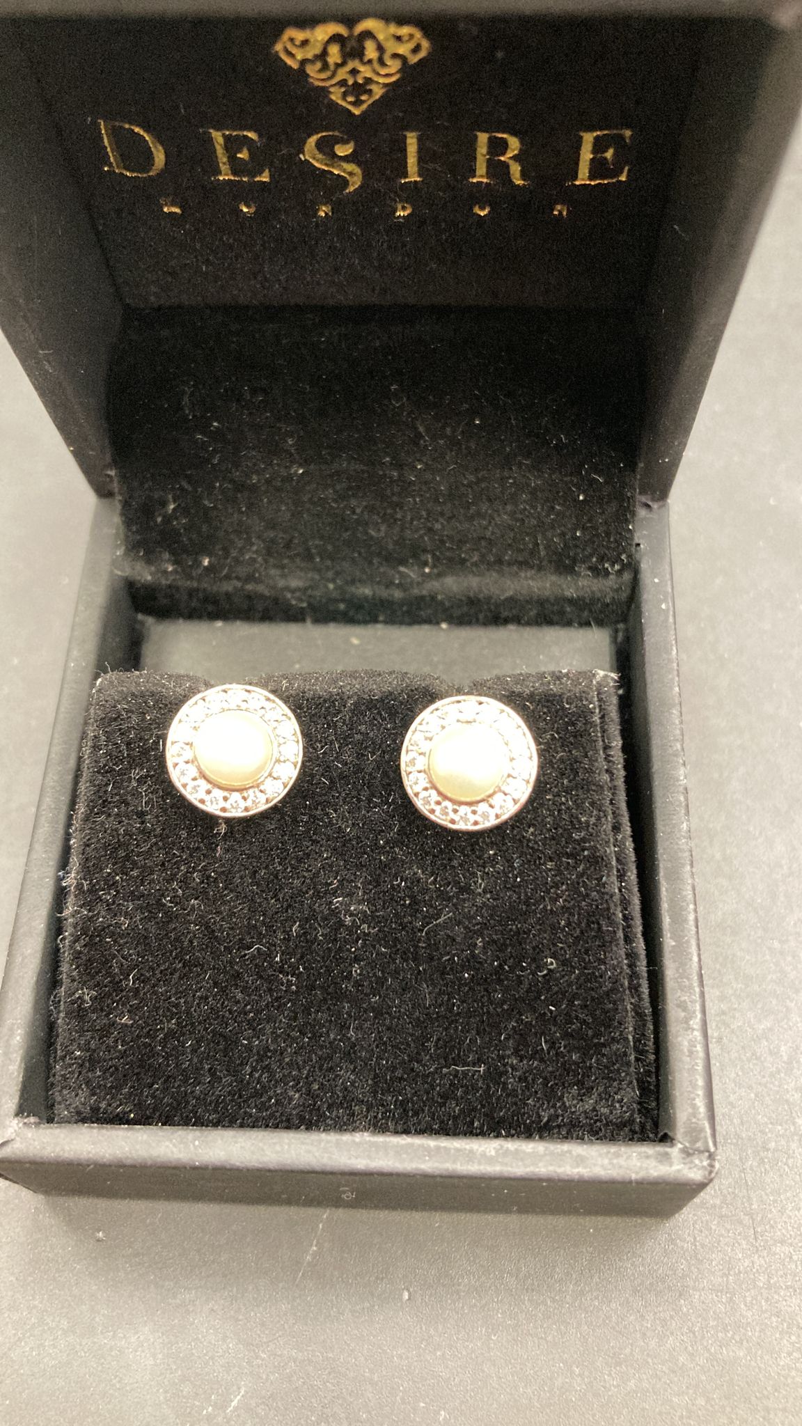 Sterling silver pearl stud earrings displayed in a black velvet jewelry box with Desire branding.
