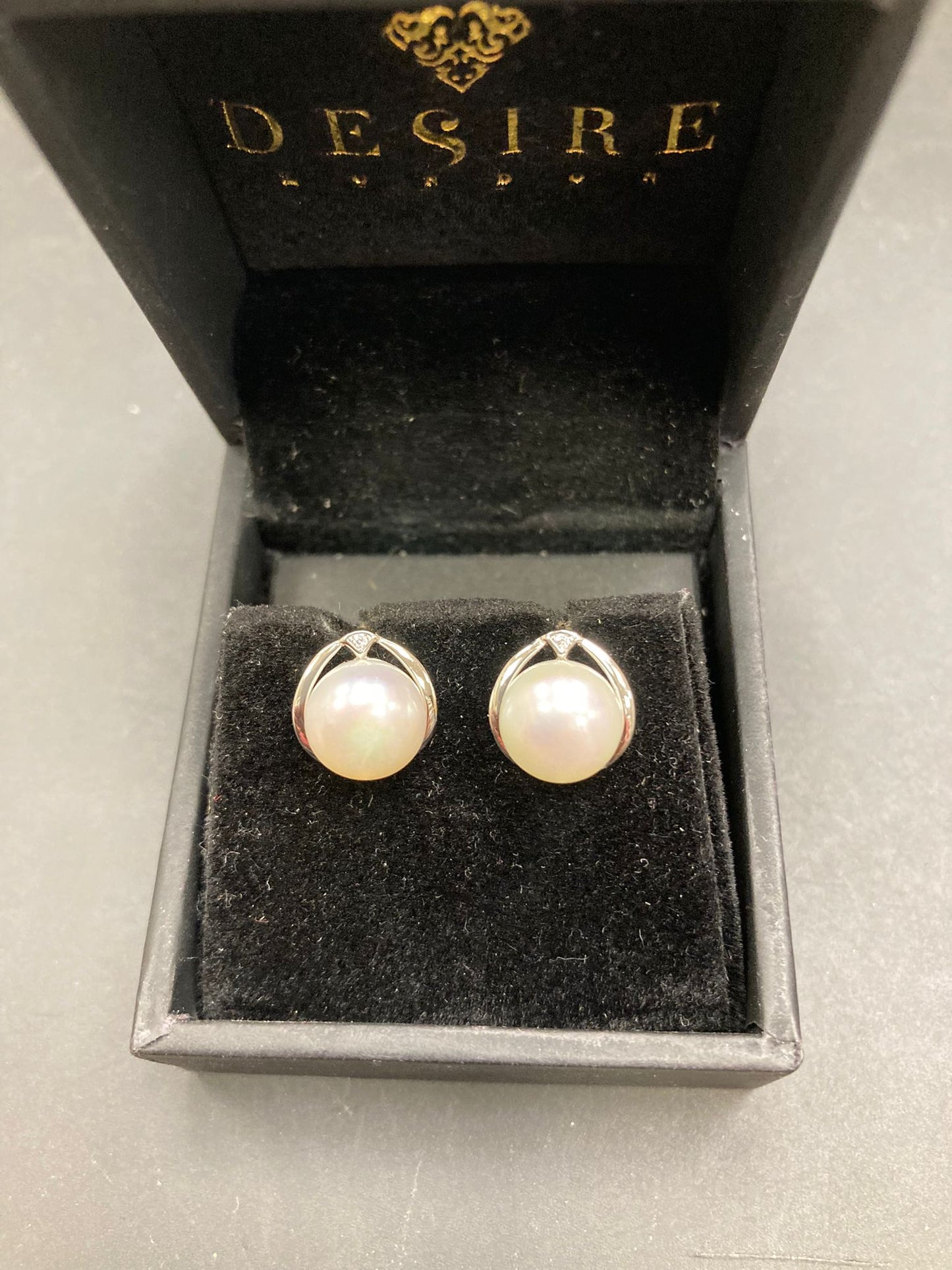 Sterling silver pearl stud earrings displayed in a black jewelry box with a velvet interior.