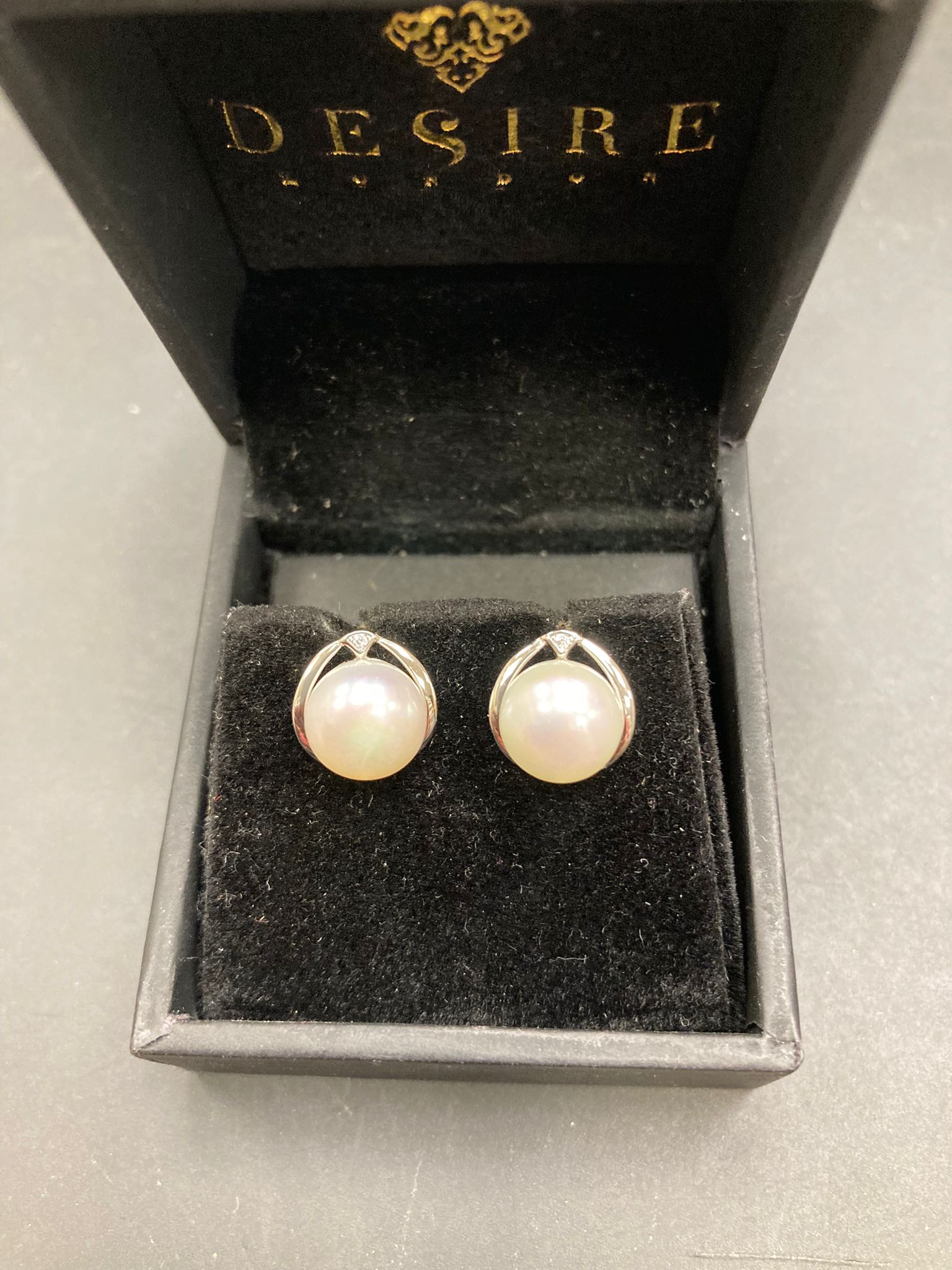 Sterling silver pearl stud earrings displayed in a black jewelry box with a velvet interior.