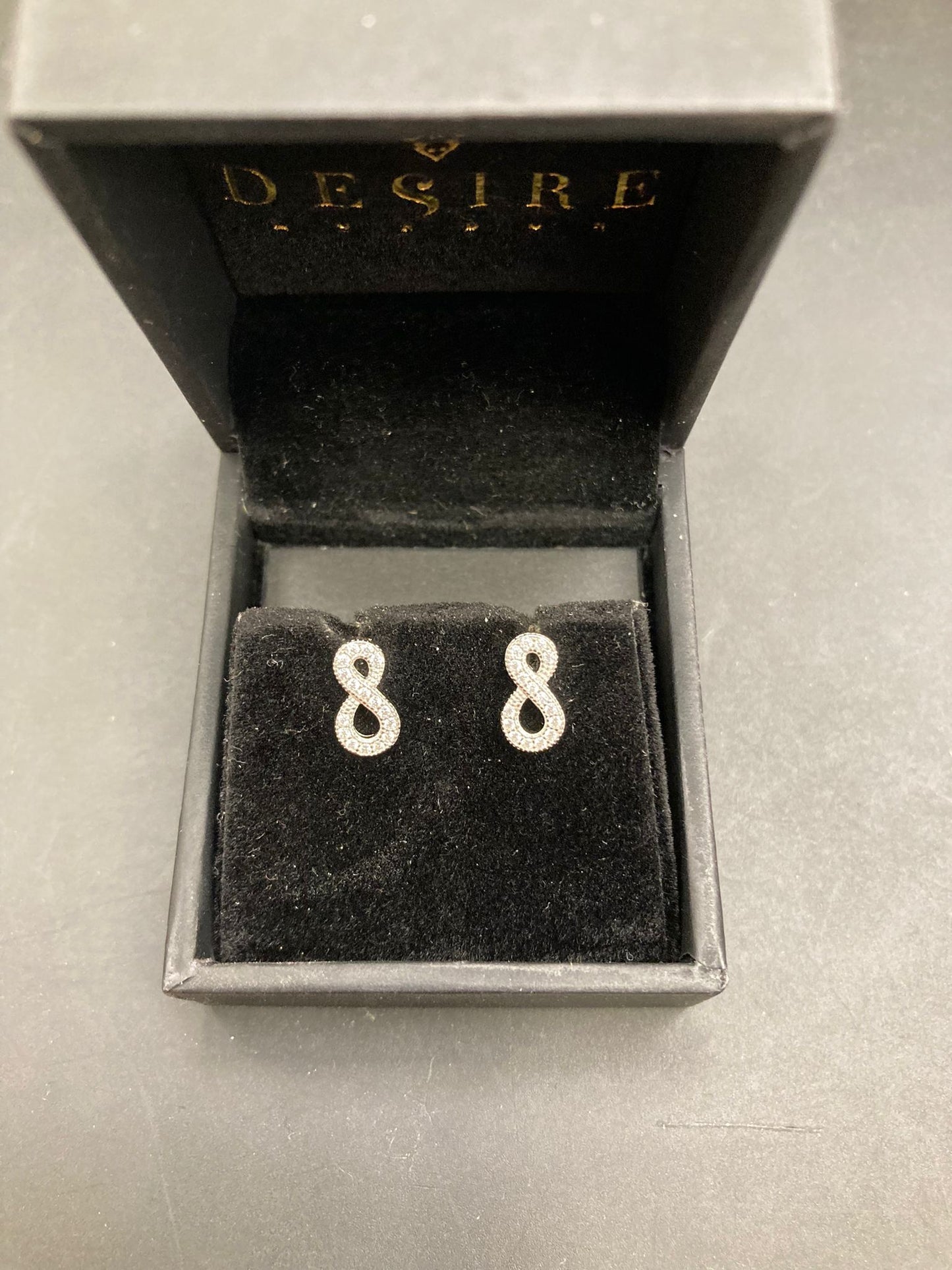 Sterling silver infinity stud earrings displayed in a Desire Jewelry box with black velvet lining.