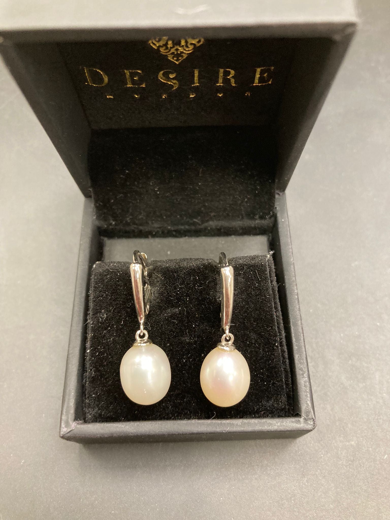 Sterling silver leverback pearl earrings displayed in a black box with the logo Desire.