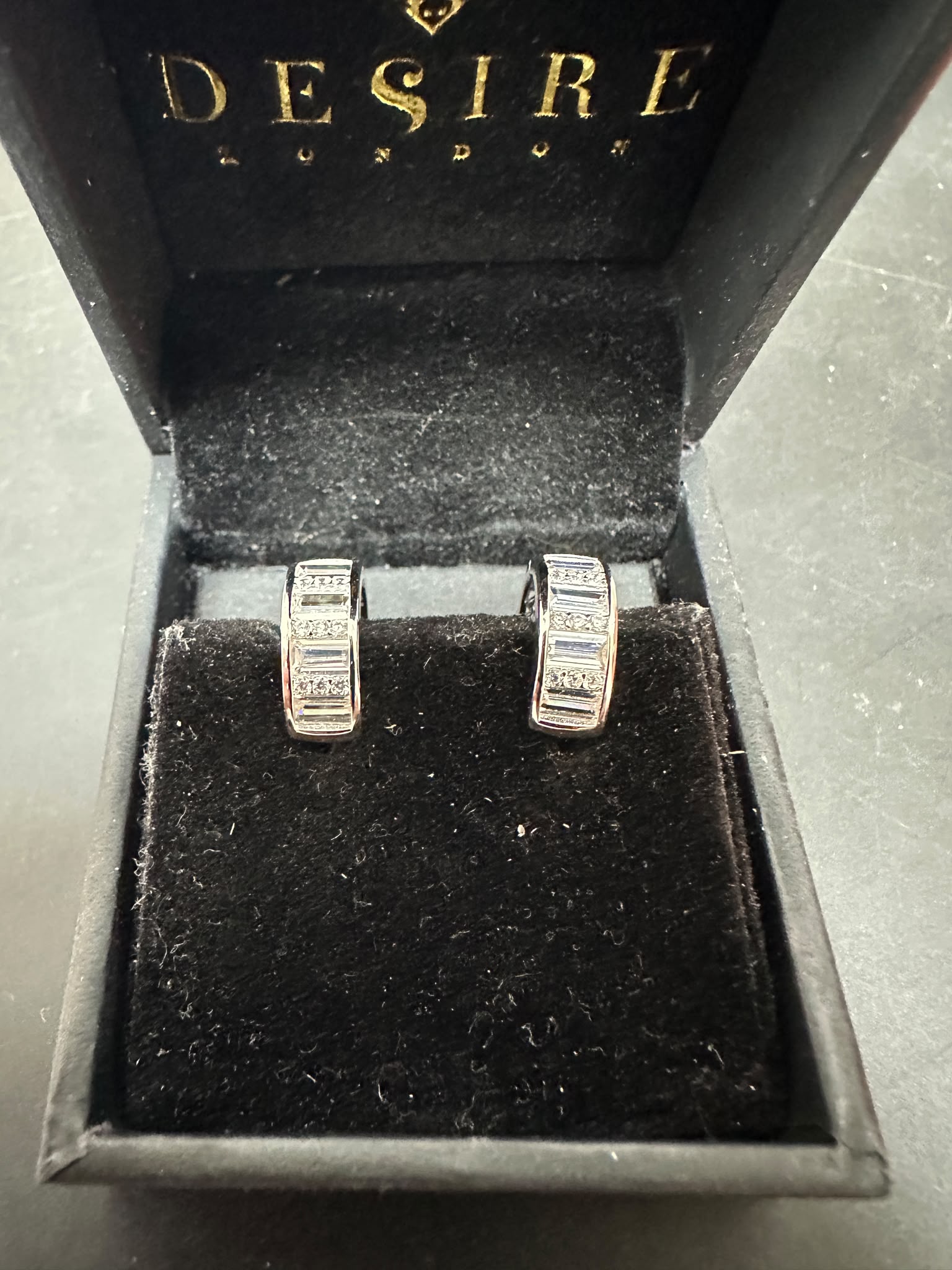 Sterling silver huggie earrings with cz stones displayed in a black jewelry box from Desire London.