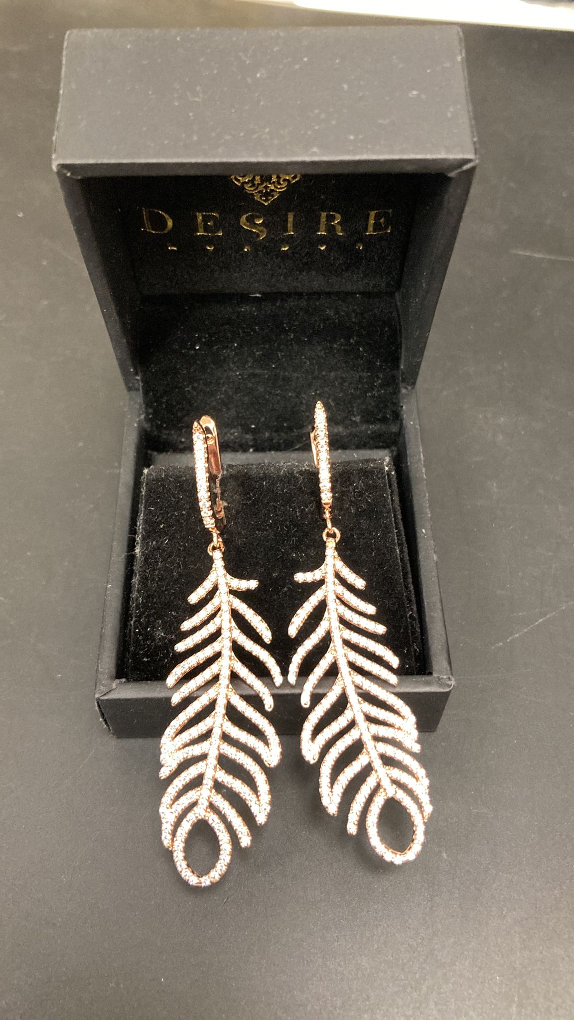 Sterling silver feather earrings displayed in a jewelry box with the Desire brand logo.