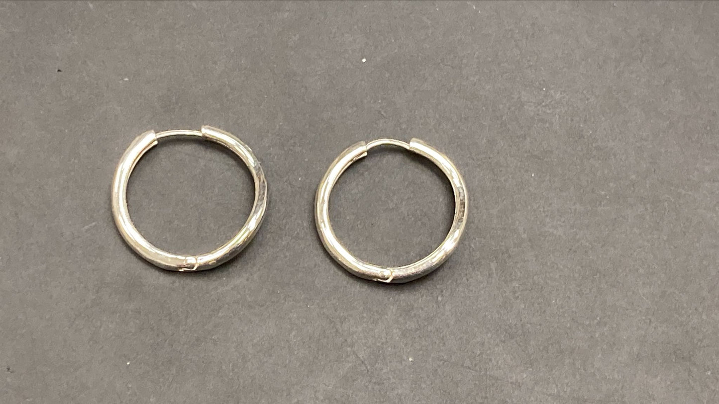 Sterling silver round hoop earrings displayed on a dark surface showcasing their sleek design and shiny finish.
