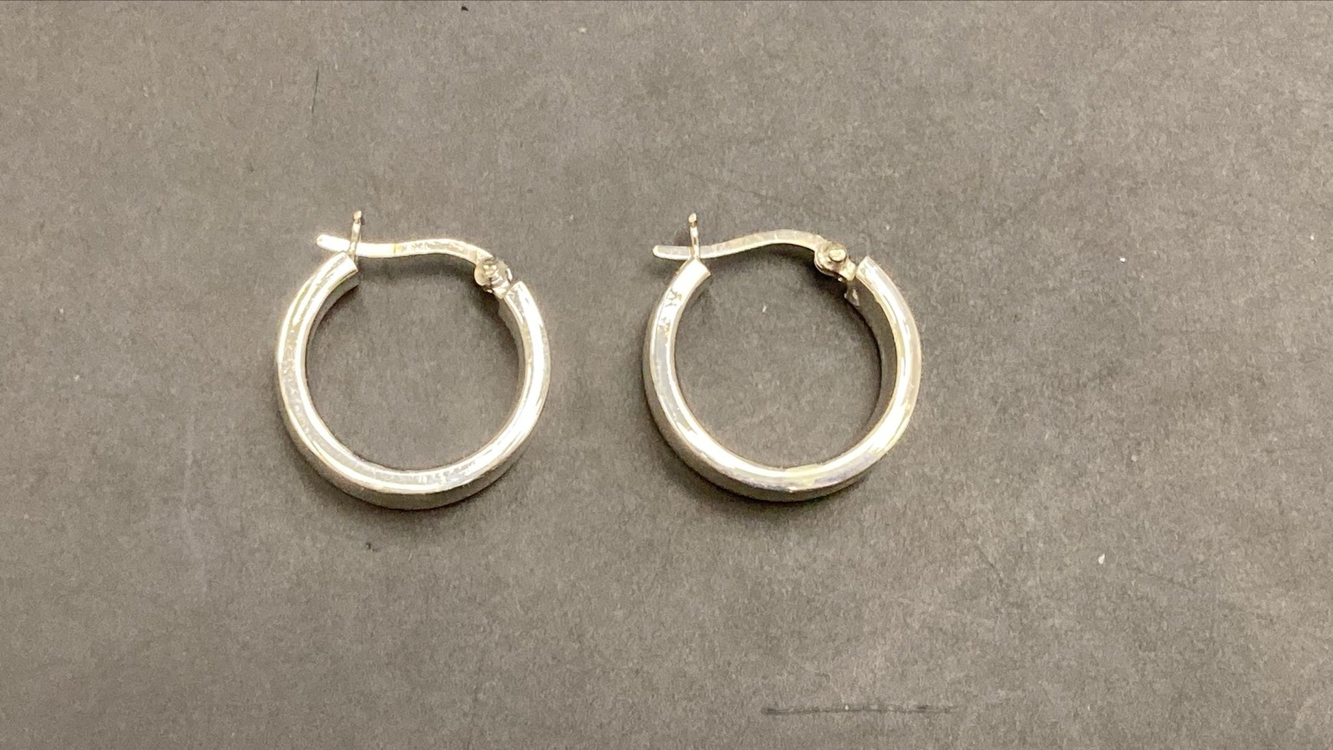 Sterling silver round hoop earrings displayed on a gray background, showcasing their polished finish and classic design.