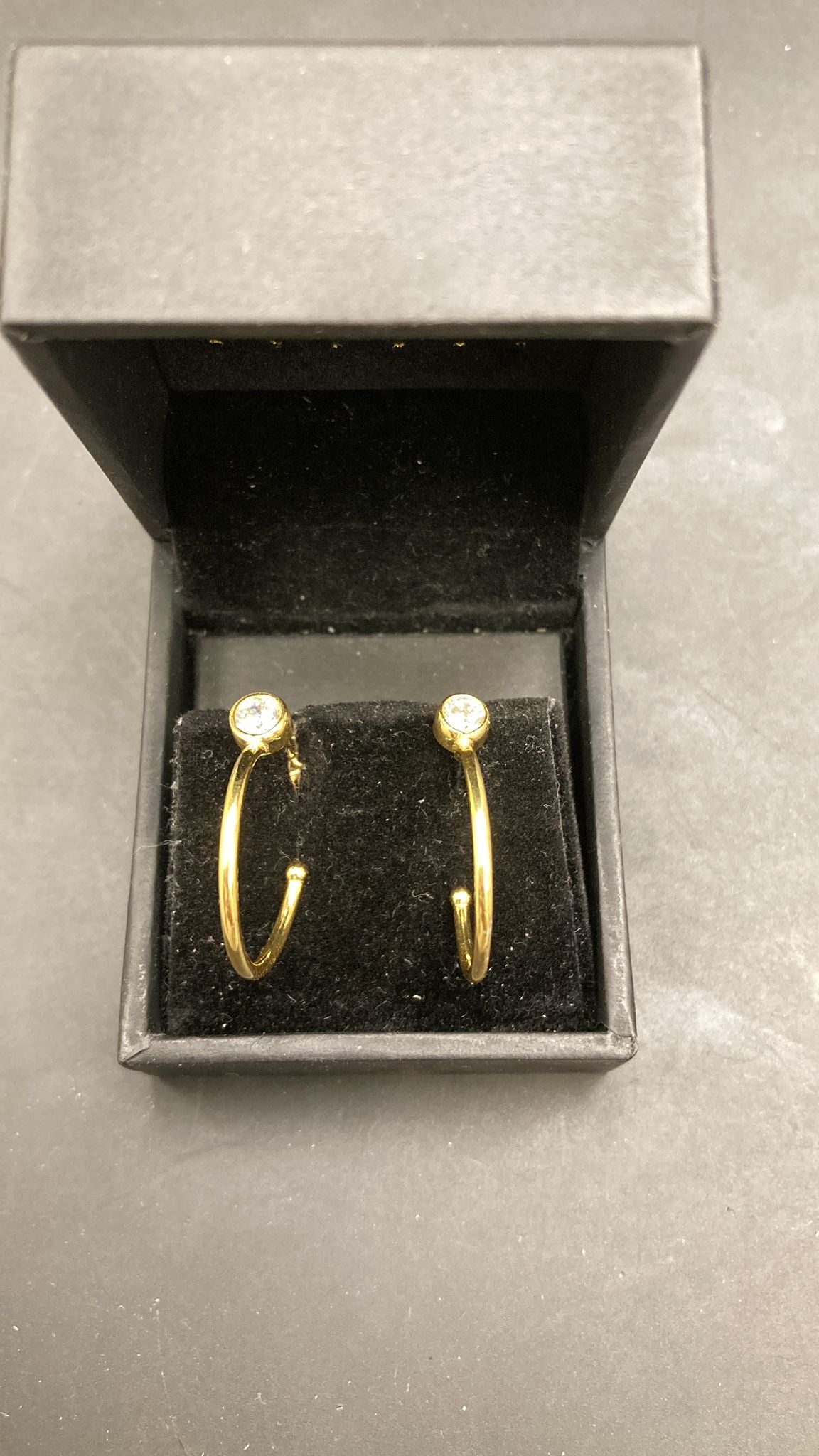 Sterling silver huggie earrings displayed in a black velvet box, featuring bezel CZ stones.