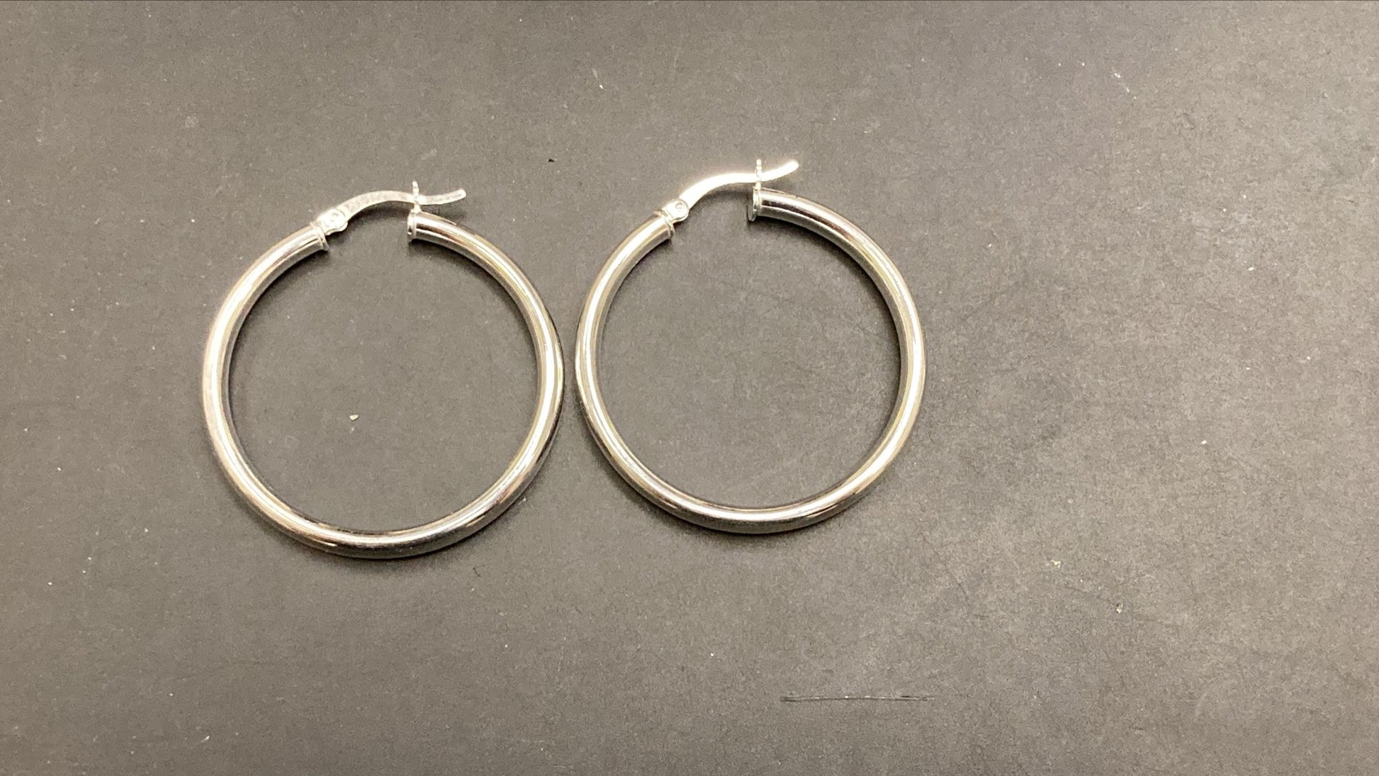 Sterling silver round hoop earrings displayed on a dark surface, featuring a classic design and polished finish.
