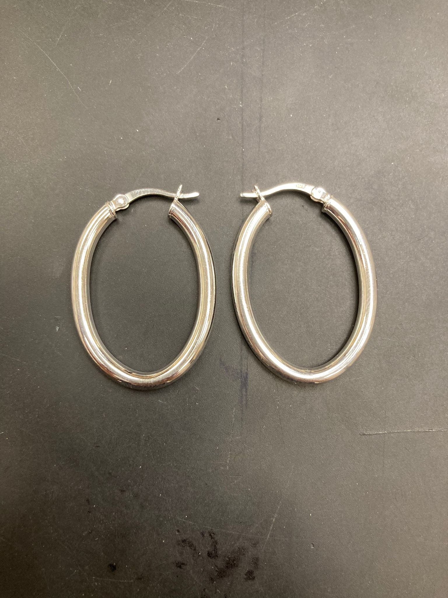 Sterling Silver Oval Hoop Earrings EP10281 displayed on a black background, showcasing the elegant design of the earrings.