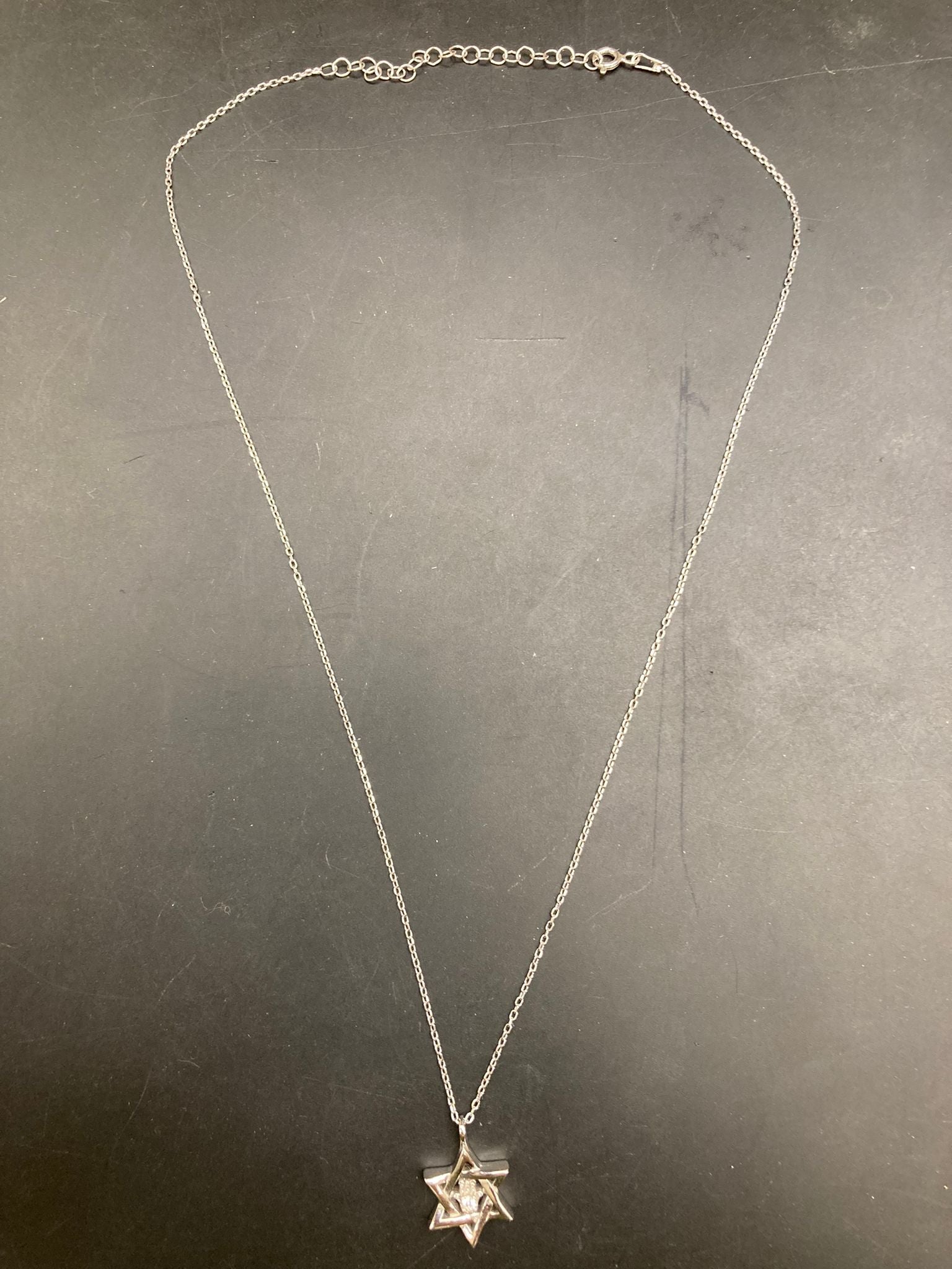 Sterling silver Star of David necklace hanging on a black background.