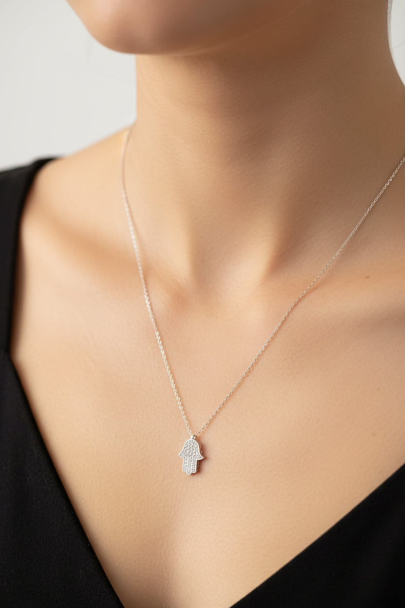 Close-up of a woman wearing a sterling silver hamsa hand necklace on a delicate chain.