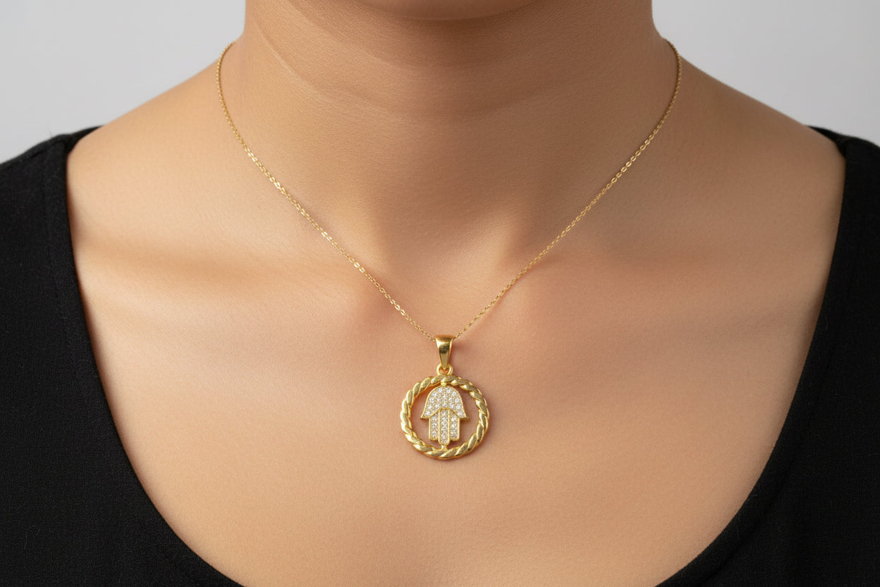Sterling silver hamsa hand pendant worn on a dainty gold chain against a black top.
