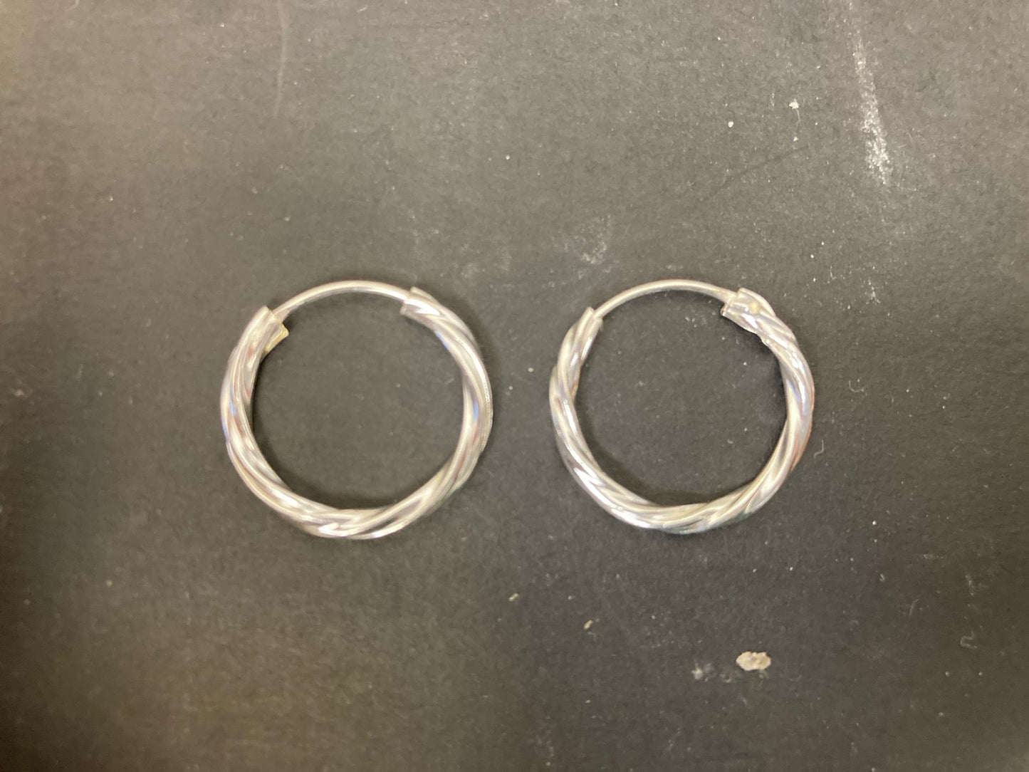 Sterling Silver Twist Hoop Earrings PE011590021 on a black background showcasing their elegant design.