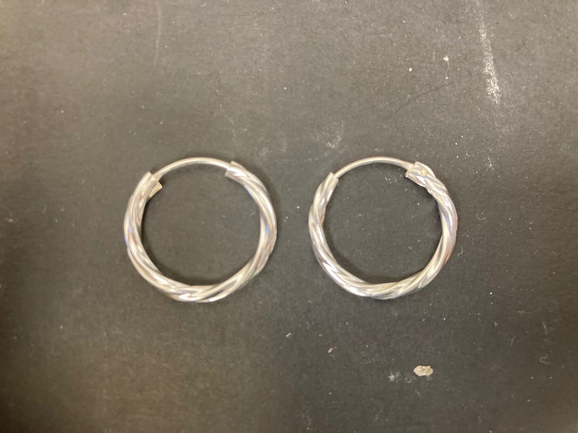 Sterling Silver Twist Hoop Earrings PE011590021 on a black background showcasing their elegant design.
