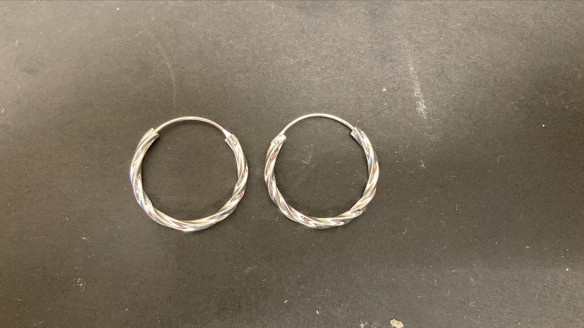 Sterling Silver Twist Hoop Earrings PE011590025 showcased on a dark surface.