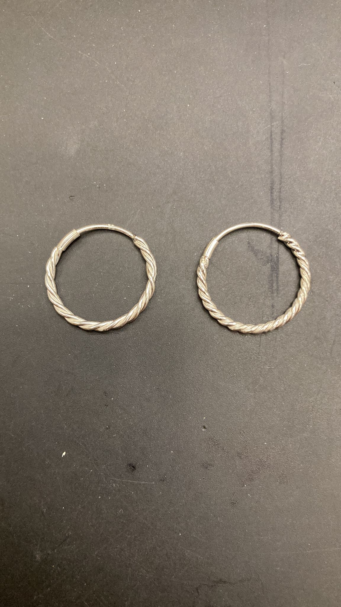 Sterling Silver Twist Hoop Earrings PE011670013 displayed on a dark background.