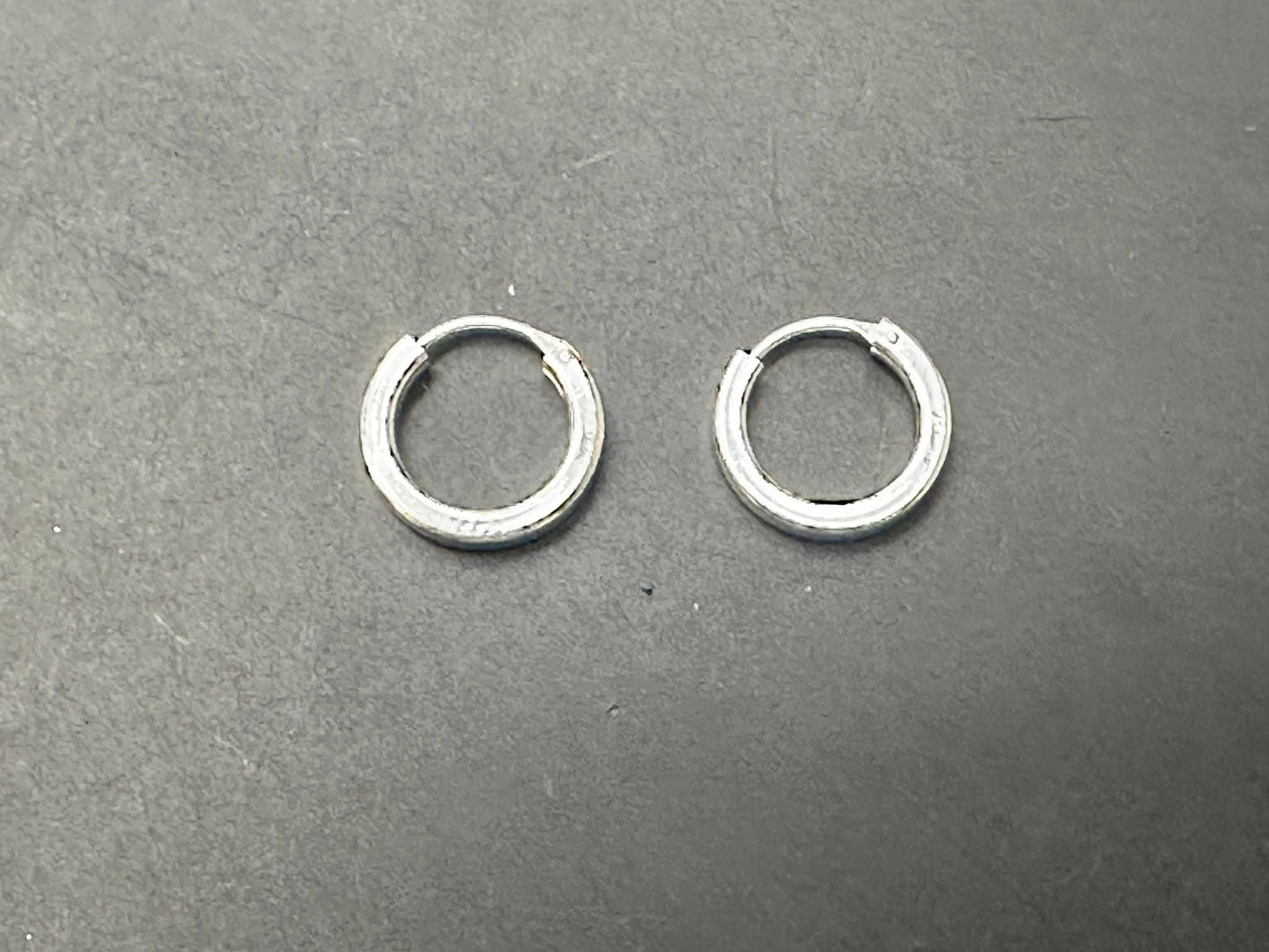Plain round sterling silver earrings displayed on a dark surface.