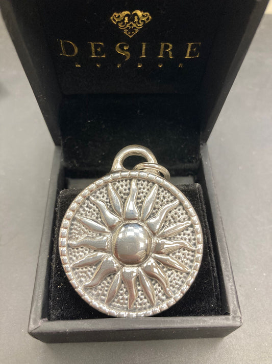 Sterling silver sun pendant displayed in a black box with the logo DE$IRE, showcasing intricate sun design.