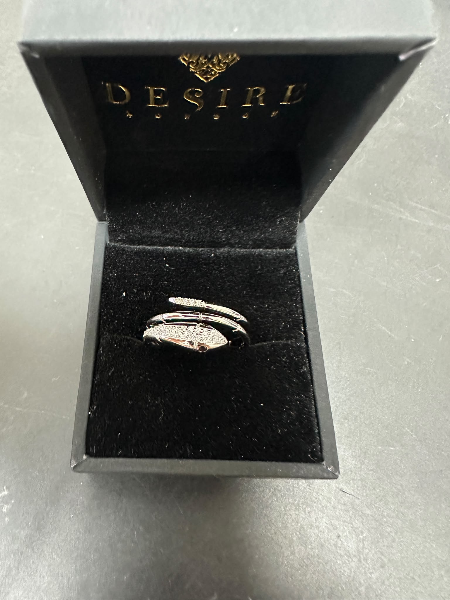 Sterling silver snake ring with cz stone displayed in a black jewelry box with DESIRE logo.